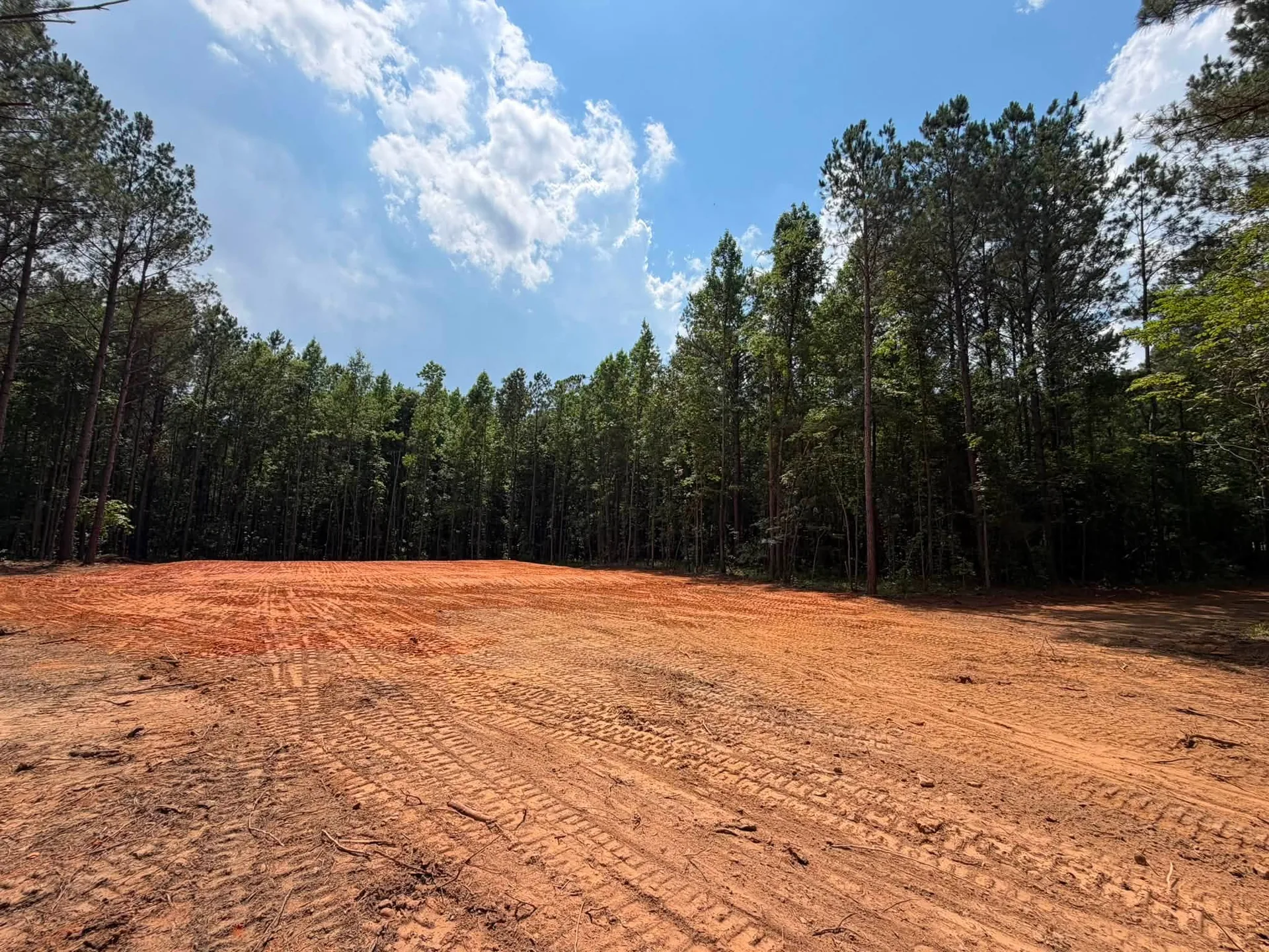Cleared red-clay property bordered by pine forest, photographed by Oak Spring Land Revival